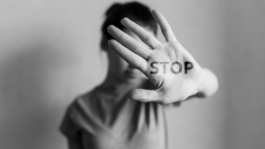 Symbolbild: Frau in abwehrender Körperhaltung mit dem auf die Hand geschriebenen Wort "Stop"