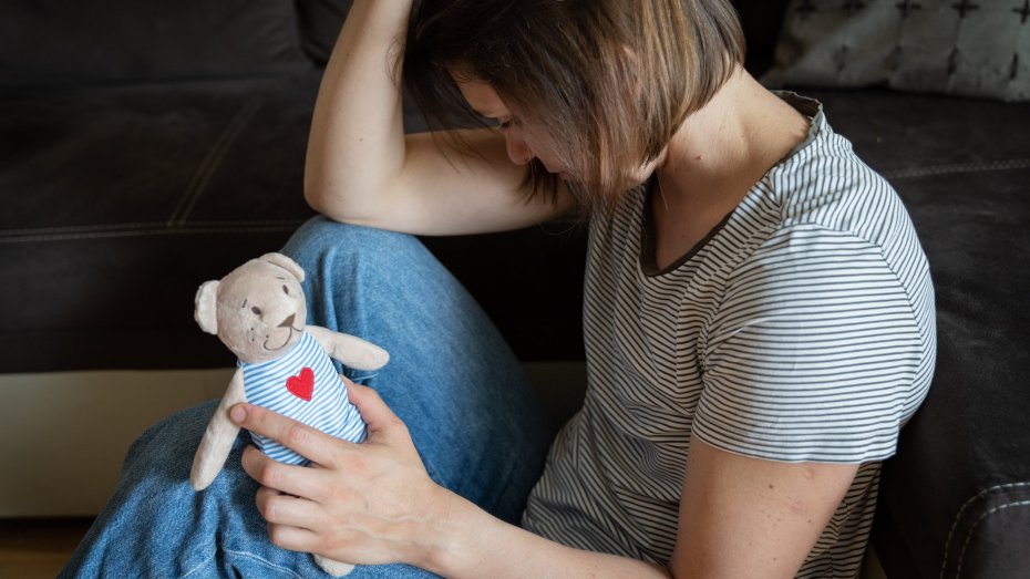 Frau nach Fehlgeburt mit traurigem Blick und Kuscheltier in der Hand