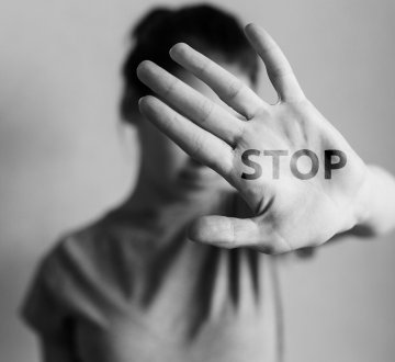 Symbolbild: Frau in abwehrender Körperhaltung mit dem auf die Hand geschriebenen Wort "Stop"