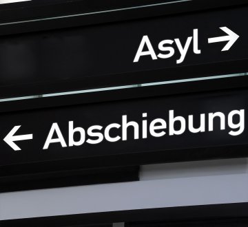 Schild mit der Aufschrift "Asyl" und einem Pfeil in eine Richtung sowie "Abschiebung" und einem Pfeil in die andere Richtung