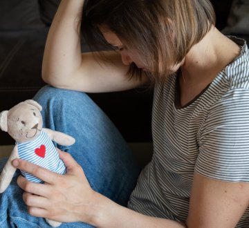 Frau nach Fehlgeburt mit traurigem Blick und Kuscheltier in der Hand