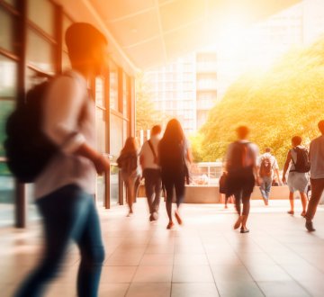 Junge Menschen in Bewegung vor einem Hochschulgebäude, im Hintergrund Sonnenstrahlen